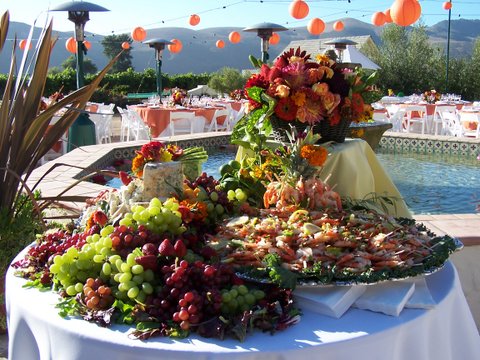 large platter of shrimp, grapes and cheese on a round table next to pool with tables in the background
