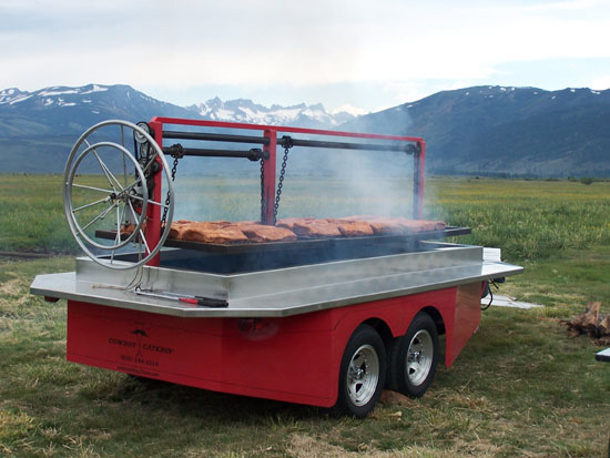 red grill with beef cooking in front of snow-capped mountains