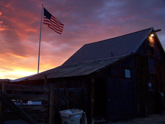 Barn with American flag flying on pole in front of beautiful sunset